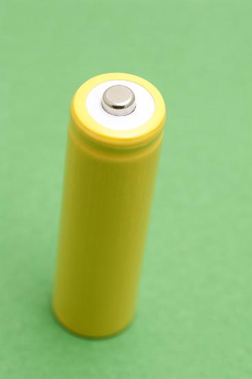 view of the positive terminal on a single unlabeled yellow battery cell on a green background