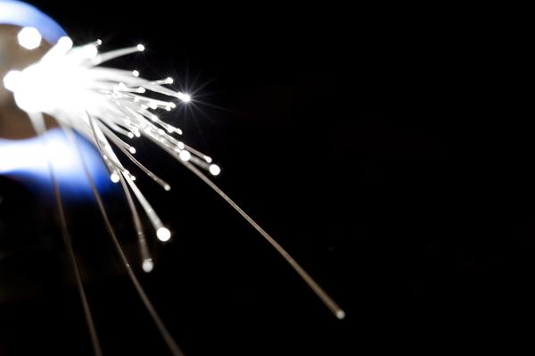 Optical fibers illuminated against a dark background showing the transmission of light and information along extruded silica filaments