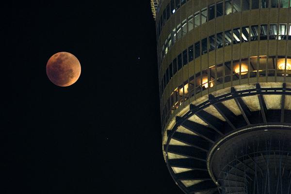 Lunar eclipse in a dark sky Lunar eclipse in a dark sky with a red colored full moon alongside an illuminated tower observsatory