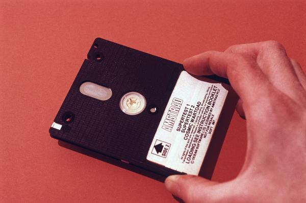 Man holding a 3 inch computer disk Man holding a 3 inch computer disk in his hand with a specification label over a red background, this type of disk was commonly used with amstrad computers in the 1980's