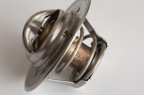 Car cooling thermostat in close-up Car cooling thermostat sitting on white surface, viewed in close-up, a bimetal strip opens the valve when the cooling watern the car is hot
