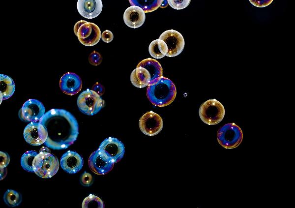 Soap bubbles reflecting light through a spectrum of beautiful colors, floating on black background, the colours are created through Iridescence or goniochromism whereby internal reflections in semi transparent surfaces create phase shifts in the reflections of ambient light